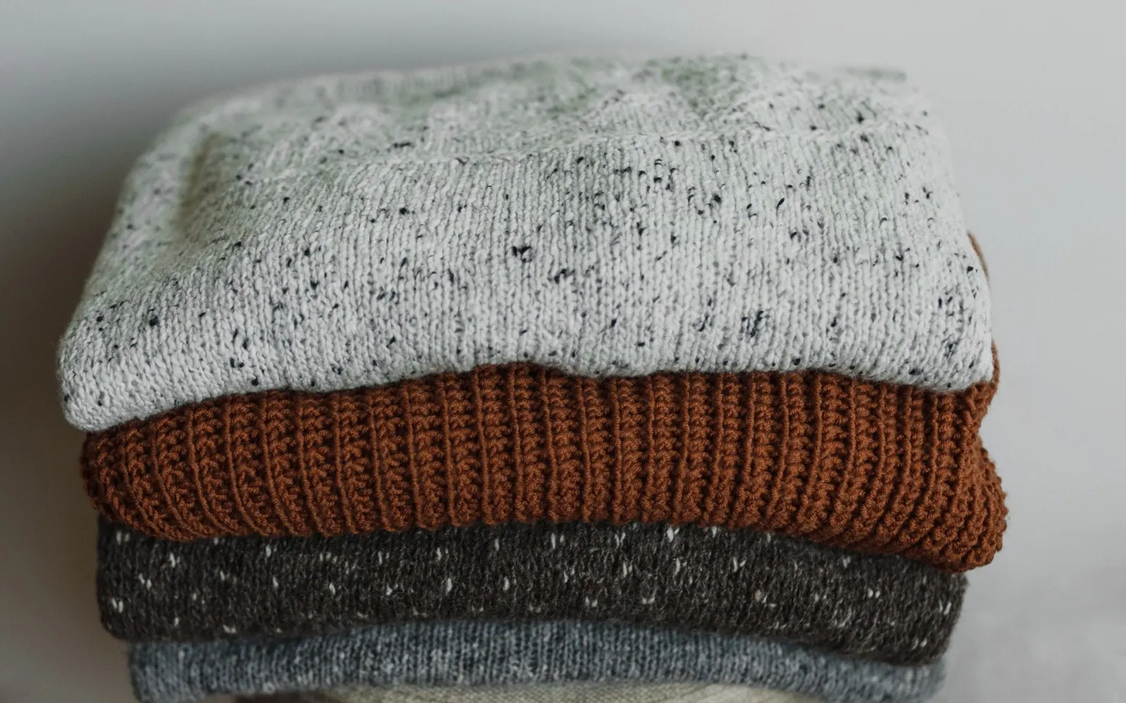 Stack of folded neutral knitwear illustrating varied knitted garment textures